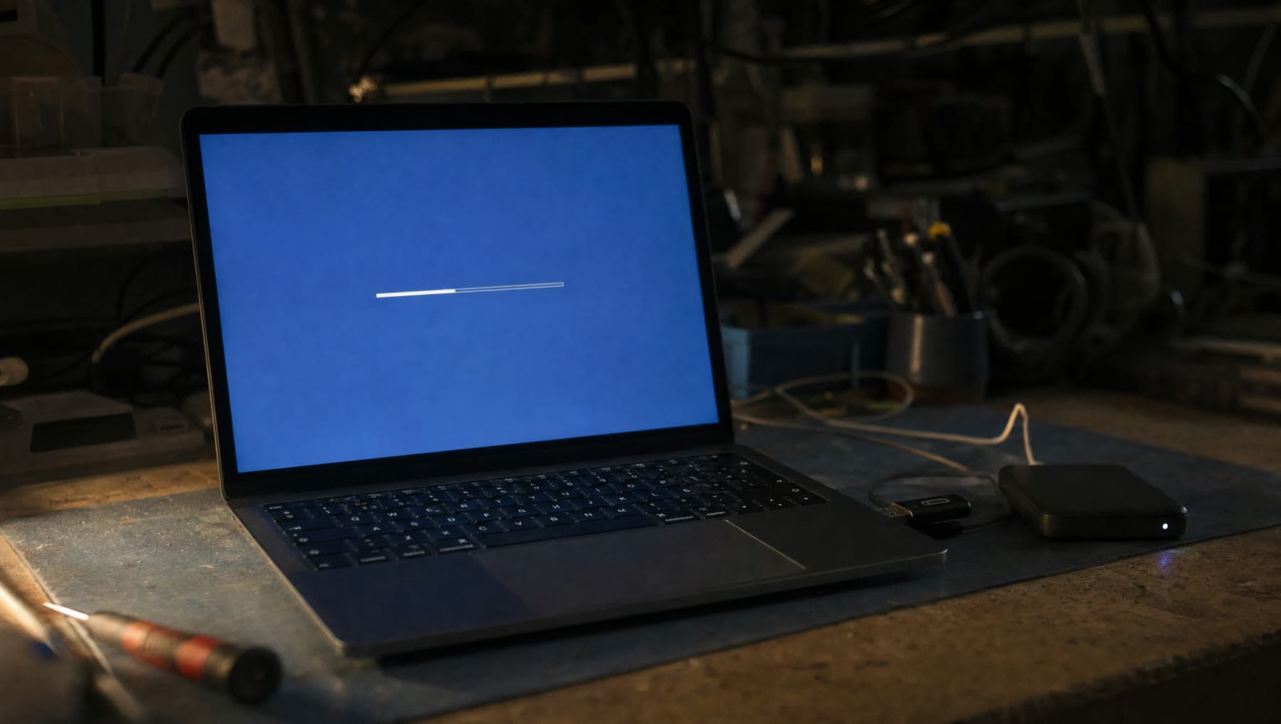 A laptop mid operating-system installation on a bench, a USB installer and a backup drive beside it.